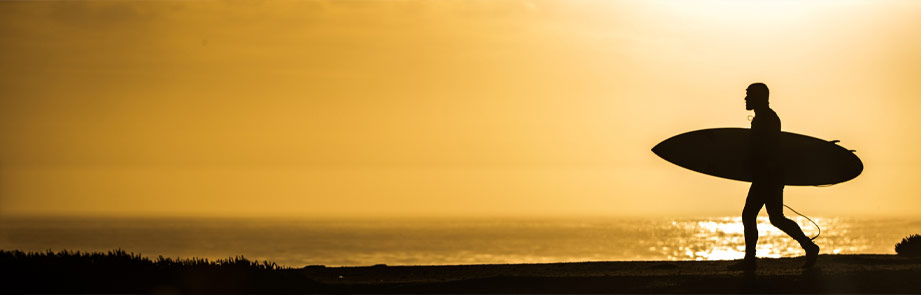 Surfer walking on the coastline at sunset